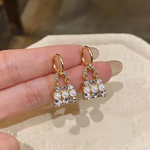 Dettaglio di orecchini a forma di borsa dorati con perle bianche e strass.