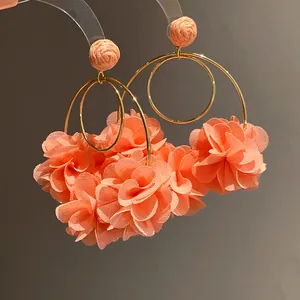 Close-up detail of elegant peach chiffon flower hoop earrings with woven raffia studs