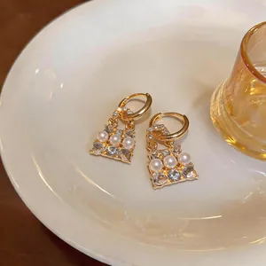 Dettaglio di orecchini a forma di borsa dorata con perle delicate e strass scintillanti.