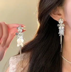Detail view of elegant silver dangle earrings with white petals and long tassels on model.