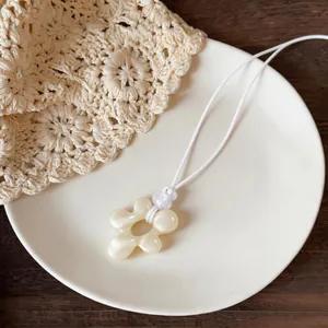 Vue détaillée du pendentif fleur en résine blanc cassé sur un cordon en cuir blanc
