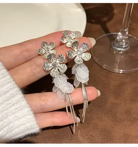 Close-up detail of elegant silver flower earrings featuring white translucent petals and tassels