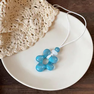 Détail d'un pendentif fleur en résine bleue avec des perles sur un cordon en cuir blanc
