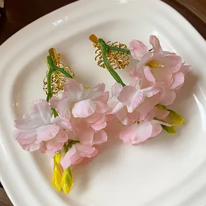 Primo piano di eleganti fermagli per capelli con fiori in tessuto rosa su piatto bianco.