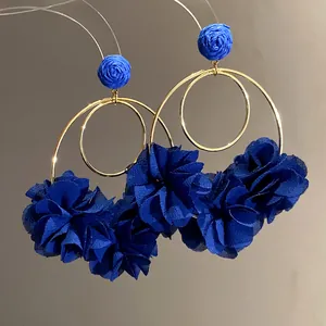 Detailed view of deep blue chiffon flower earrings with golden hoops and raffia accents