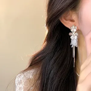 Detailed view of silver flower earrings with white petals and long tassels worn on ear