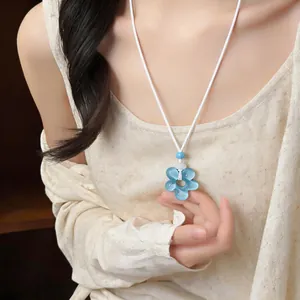 Détail d'un pendentif fleur en résine bleue sur un collier en cordon blanc porté par un mannequin