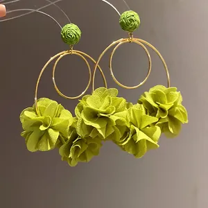 Detailed macro view of green chiffon flower and raffia ball drop earrings on gold hoops