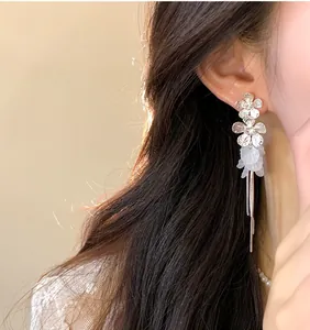 Close-up of silver tassel earrings with white petal accents on ear