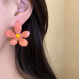 Close-up macro view of peach resin flower stud earring with yellow center worn on ear