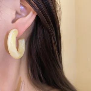 Detailed view of cream yellow resin hoop earring with marble texture on an ear
