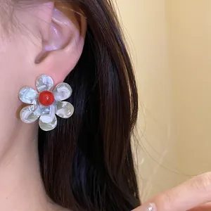 Macro detail of marbled resin flower stud earrings featuring a vibrant red center focal point