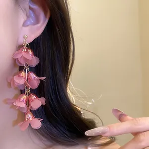 Detailed macro view of long pink floral drop earrings worn on ear with soft lighting