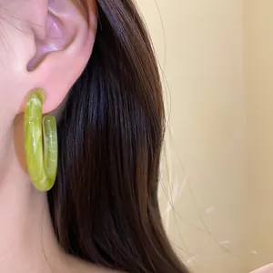 Macro detail of a light green resin hoop earring with marble pattern worn by a model