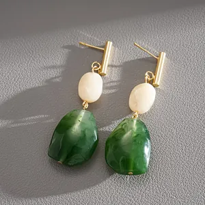 Close-up of vintage drop earrings with green and cream resin stones and gold accents.