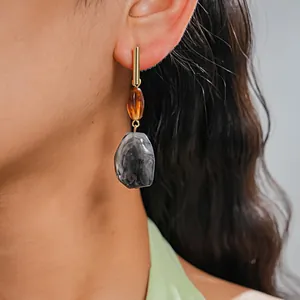 Close-up of retro resin geometric earrings with marbled grey and amber pendants