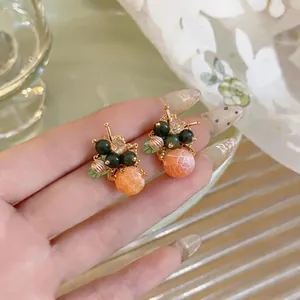 Dettaglio di orecchini a grappolo di frutta con perline arancioni e verdi sulla mano.