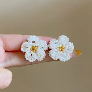 Dettaglio di orecchini a forma di fiore di camelia in perline bianche e oro.