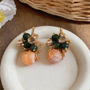 Dettaglio macro di orecchini a fiore unici con perle verdi e arancioni screpolate.