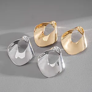 Close-up of abstract irregular hollowed-out metal stud earrings in gold and silver