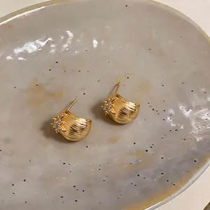 Gros plan sur des puces d'oreilles dorées en forme de coquillage avec fleurs en zircon