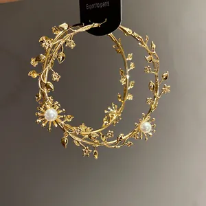 Makroansicht goldfarbener Creolen mit floralen Zweigen und einem Perlenakzent