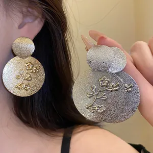Detail of metallic textured round earrings with embossed flower pattern.