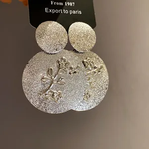 Detailed view of silver-tone textured round earrings with embossed floral branch design