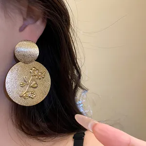 Close-up of elegant gold textured round earrings with embossed flower design