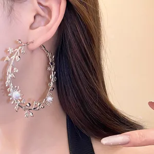 Nahaufnahme von eleganten silbernen Zweig- und Perlenblumen-Creolen an einem Modell.