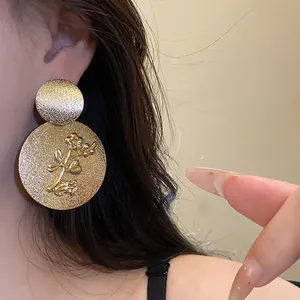 Detailed view of a gold textured round earring with floral relief on a person's ear.