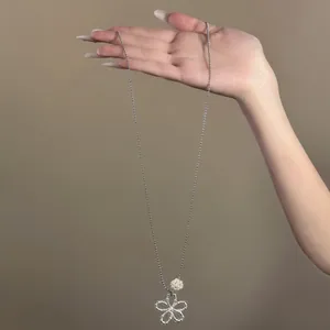 Hand displaying a delicate silver-toned hollow flower pendant necklace with pearl