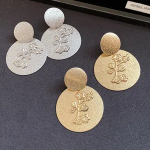 Detailed view of textured gold and silver round earrings with embossed flower designs.