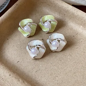 Primo piano di eleganti orecchini a fiore con perle e finitura in smalto dai riflessi perlati.