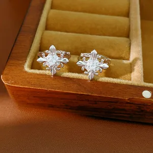 Close-up detail of silver fleur-de-lis hoop earrings with sparkling zircon inlay in a wooden box.
