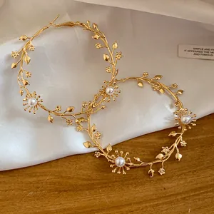 Nahaufnahme von goldenen Creolen mit filigranen Zweig-, Blumen- und Perlendetails