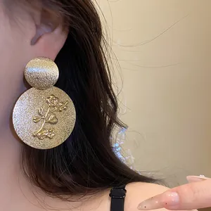 Close-up of golden textured metal floral embossed earrings on model's ear