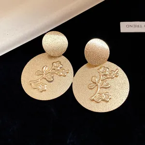 Macro view of golden metal round earrings with textured floral branch relief design