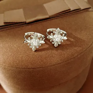 Detailed macro view of silver hoop earrings with zircon fleur-de-lis cross design