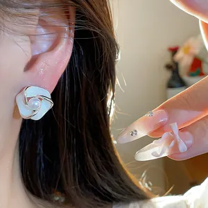 Primo piano dettagliato di un orecchino a perno a fiore in smalto bianco con perla sull'orecchio.