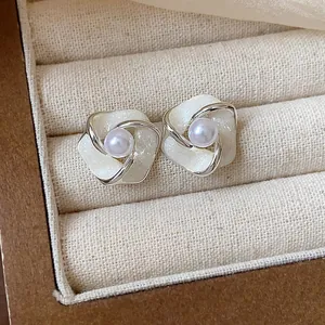 Primo piano di eleganti orecchini a lobo a fiore con smalto crema e perla centrale