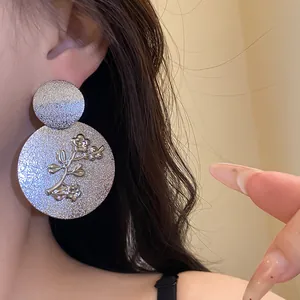 Detailed view of silver-toned textured round earrings with floral engraving on model
