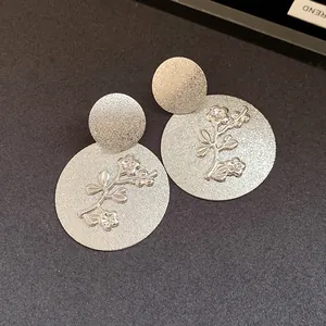 Detailed macro view of silver frosted round earrings with elegant embossed floral pattern