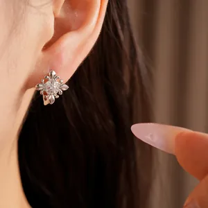 Close-up view of a shimmering silver fleur-de-lis cross earring set with zircons on an ear