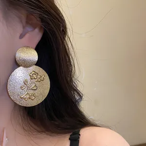 Detailed view of large gold-tone metal earrings with floral relief on a model.
