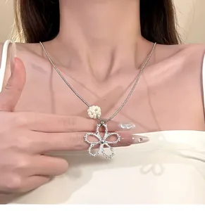 Detailed view of a silver hollow flower pendant necklace with pearl on model's neck.