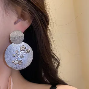 Close-up detail of a textured silver round flower earring worn by an Asian model