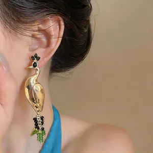 Detail of vintage gold peacock dangle earring with crystal accents on female ear.