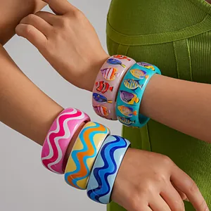 Detailed view of colorful resin bangles with wavy and tropical fish prints on arm.