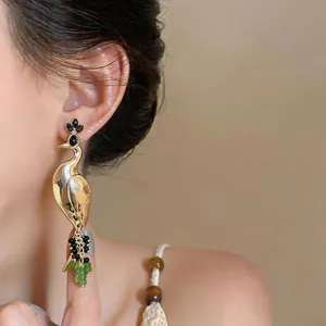 Close-up of vintage gold peacock earrings with emerald green and black beads worn on the ear.